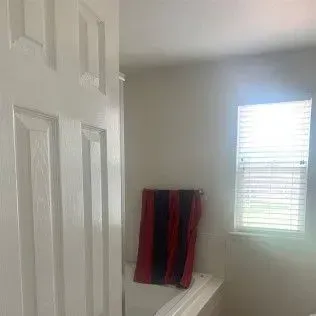 White door opening into a bathroom with a window and a red, black, and blue towel.