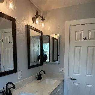 Bathroom with mirrors, sinks, and white door. Black fixtures and gray walls.