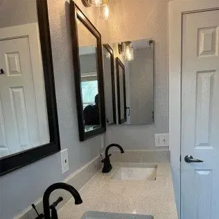 Bathroom with two sinks, mirrors, and a door, featuring black fixtures and light gray walls.