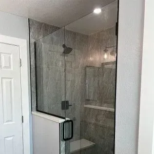 Glass shower enclosure in a bathroom with gray tiled walls.