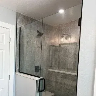 Glass shower enclosure with black hardware, gray tile, and a white door.