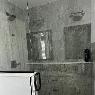 Bathroom with a glass shower door, gray tiled walls, vanity, mirror, and shower fixtures.