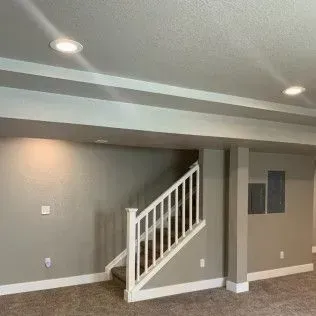 Interior view of a basement with stairs, gray walls, recessed lighting, and white trim.