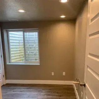 Empty beige room with a window, white trim, and a closed door.