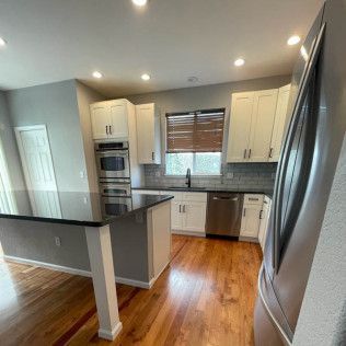 Modern kitchen with white cabinets, stainless steel appliances, and a black countertop island.