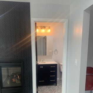 View through an open doorway into a bathroom with dark blue vanity and silver light fixture.
