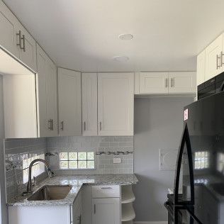 White kitchen with cabinets, sink, and a black microwave.