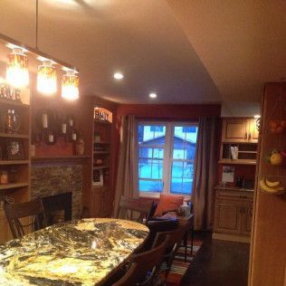 Kitchen with large granite countertop island, fireplace, built-in shelves, and window with curtains.