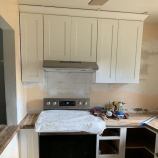 Kitchen remodel in progress: white cabinets, range hood, and stove installed. Unfinished walls and countertop.