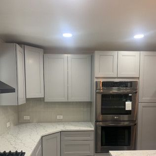 Kitchen with white and gray cabinets, stainless steel oven, and light-colored countertops.