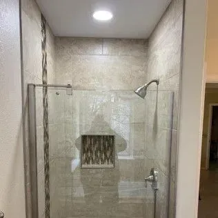 Shower with glass doors and beige tile, featuring a showerhead and faucet.