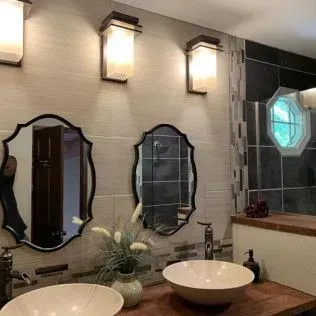 Bathroom with two mirrors over sinks, three wall sconces, and a shower area.