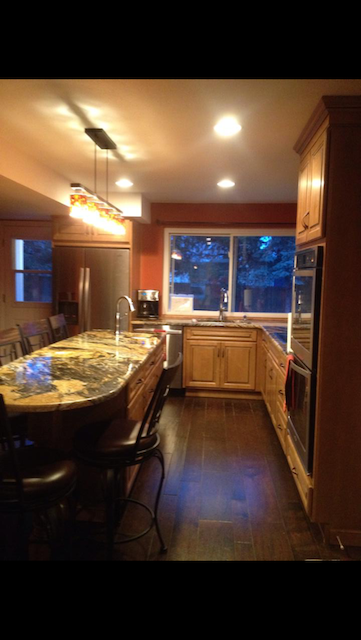 Kitchen with wood cabinets, dark floors, granite island, and stainless steel appliances.