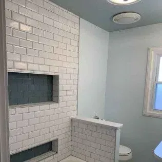 Bathroom with white subway tile shower, blue accent, and recessed storage.