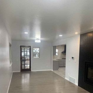 Living room with hardwood floors, a dark door, and a fireplace. Light gray walls and ceiling with recessed lighting.