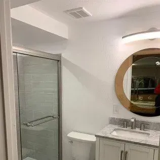 Bathroom with a shower, toilet, vanity, and round mirror.