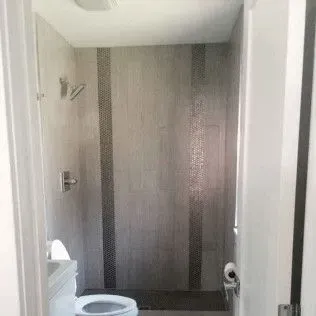Bathroom interior with a shower, toilet, and gray tiled walls.