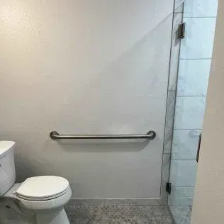 Bathroom with toilet, grab bar on wall, and glass shower door.