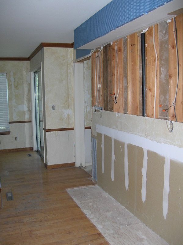 Interior view of a room under renovation; exposed wooden studs, drywall partially installed, blue wallpaper above.