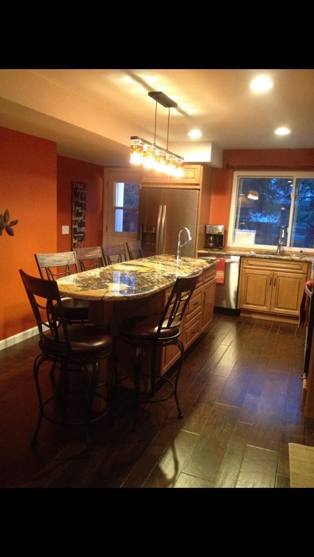 Kitchen with orange walls, island with seating, dark wood floors, and natural light.
