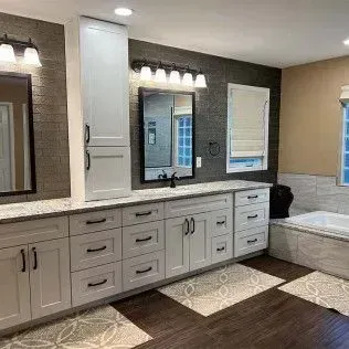 Bathroom with white cabinets, dark countertops, dark backsplash, a tub, and patterned floor mats.