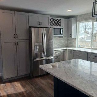 Modern kitchen with gray cabinets, stainless steel refrigerator, and granite countertop.