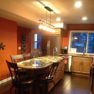 Kitchen with orange walls, a granite-topped island, wooden cabinets, and stainless steel appliances.