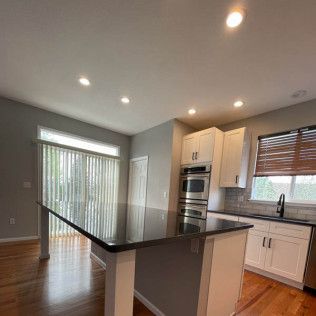 Modern kitchen with a black island, white cabinets, and wood floors. A window with blinds is on the left.