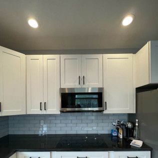 White kitchen cabinets above a black countertop with a microwave, lights, and backsplash.