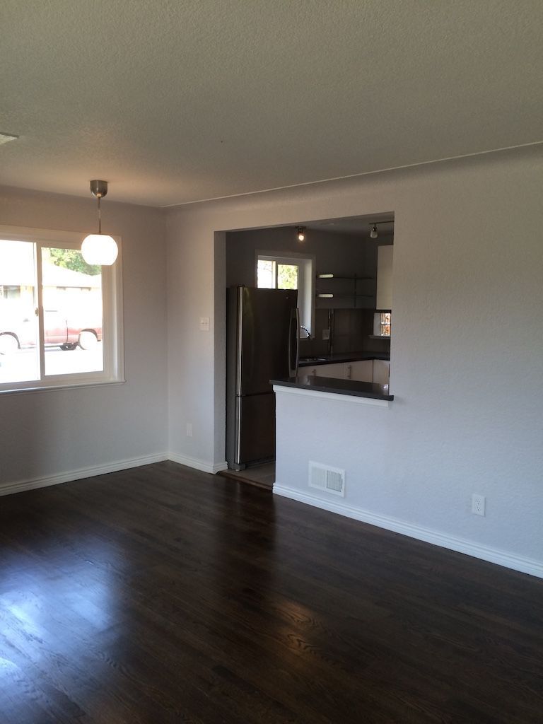 Living room with dark wood floor, light gray walls, and a view into the kitchen.