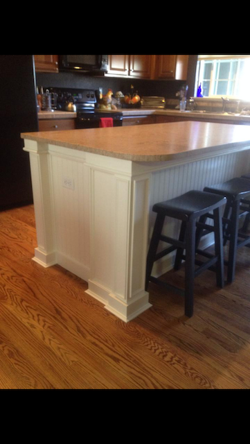 Kitchen island with white paneling, wooden floor, and black stools.