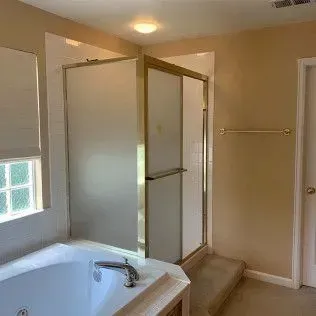 Bathroom with a bathtub, frosted glass shower, and beige walls.