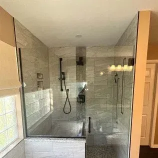 Shower with gray tiles, glass door, and black fixtures.