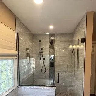 Modern bathroom with gray tiled walls, glass shower, and black fixtures.