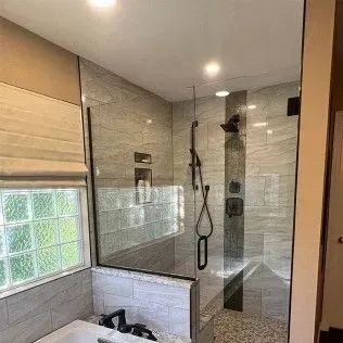 Shower with glass walls, tiled interior, black fixtures, and a pebble floor.