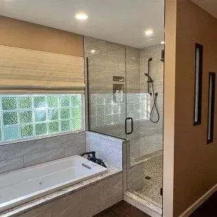 Bathroom with a tub and a glass-enclosed shower. Gray tile, beige walls, and a window with block glass.