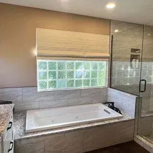 Bathroom with a built-in tub, tiled surround, glass block window, and a glass shower.