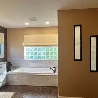 Bathroom interior: bathtub near a window with glass blocks; brown walls and wood floor.