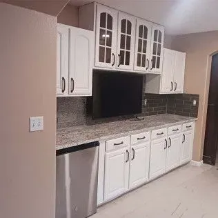 White kitchen cabinets with granite countertops, stainless steel appliances, and a mounted TV.