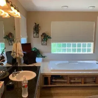 Bathroom with a sink, bathtub, and window with a shade; neutral colors and decorative plants.
