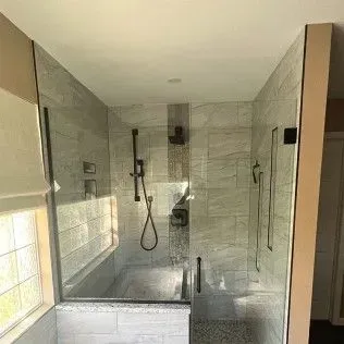 Modern shower with glass walls, black fixtures, and gray tile.