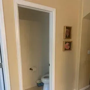 Open doorway leading to a small bathroom with a toilet and a wall-mounted paper towel holder.