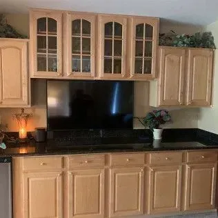 Kitchen with light wood cabinets, black countertop, TV, and decorative greenery.