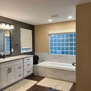 Bathroom with a white bathtub, white vanity, and a window with glass blocks.