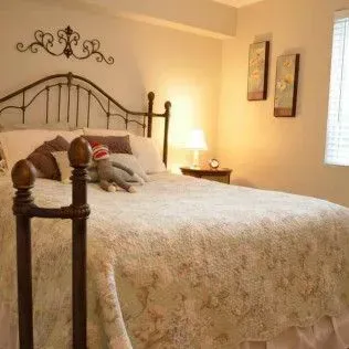 Bedroom with wrought-iron bed, floral quilt, pillows, lamp, wall art, and a stuffed animal.