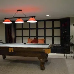 Pool table in a game room with red lighting, cushioned seating, and a bar stool.