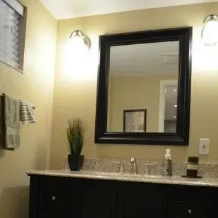Bathroom with black framed mirror, vanity, lights, and beige walls.