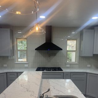 Modern kitchen with grey cabinets, quartz countertops, black range hood, and windows.