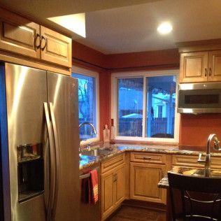 Kitchen with light wood cabinets, stainless steel refrigerator, and orange walls.