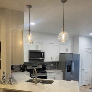 Kitchen with pendant lights, white cabinets, stainless steel appliances, and a marble countertop.